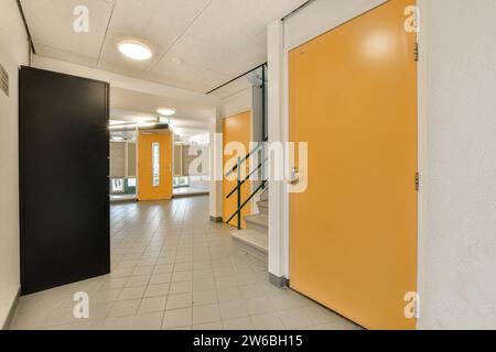 Leerer langer Flur mit gelben Türen und weißem Fliesenboden im beleuchteten modernen Bürogebäude Stockfoto