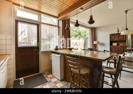 Minikühlschrank unter Holztheke in kleiner Küche des modernen Hauses mit Wohnzimmer im Hintergrund Stockfoto