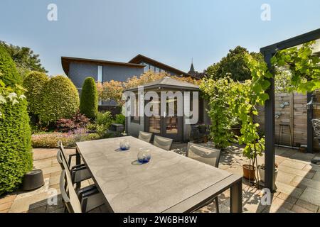 Langer Esstisch und Stühle im geräumigen Garten des modernen Hauses mit Schuppen und Bäumen Stockfoto