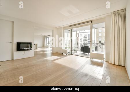 Ein geräumiges, gut beleuchtetes, modernes Wohnzimmer mit Hartholzfußboden, offenen Balkontüren und minimalistischem Dekor. Stockfoto