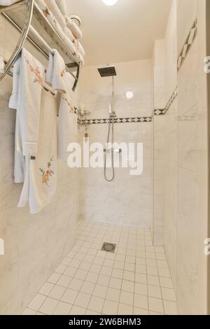 Handtücher hängen auf einem Regal in einer kleinen Duschkabine des modernen Apartments mit gefliestem Boden und Wänden Stockfoto