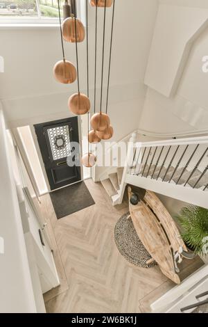 Hohe Pendelleuchten hängen über dem Eingangsflur mit Treppe und Holzbank in der Villa Stockfoto