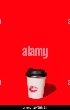 Weiße Kaffeetasse zum Mitnehmen mit einem schwarzen Deckel und einer Lippenstift-Kiss-Markierung vor einem leuchtend roten Hintergrund, die einen Farbakzent bietet. Stockfoto