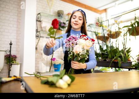 Positive junge Blumenläuferin, die einen Blumenstrauß aus Rosen-Chrysanthemen und gypsophila-Blüten anordnet, während sie im Blumengeschäft arbeitet Stockfoto