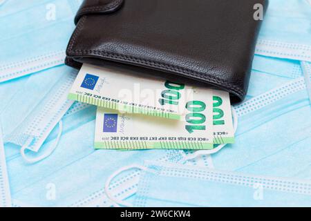 Schwarze Herren Brieftasche mit Euro Geld innen auf den blauen Einweg-medizinischen Gesichtsmasken. Handel mit medizinischen Masken. Unternehmen während einer Pandemie oder Epidemie Stockfoto