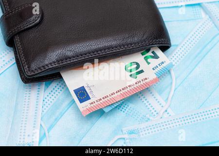 Schwarze Herren Brieftasche mit Euro Geld innen auf den blauen Einweg-medizinischen Gesichtsmasken. Handel mit medizinischen Masken. Unternehmen während einer Pandemie oder Epidemie Stockfoto