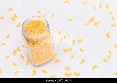 Ungekochte Chifferi Rigati Pasta in Glasglas auf weißem Hintergrund. Fett und ungesunde Lebensmittel. Verstreute Klassische Trockene Makkaroni. Italienische Kultur und Küche. Rohe Pasta Stockfoto