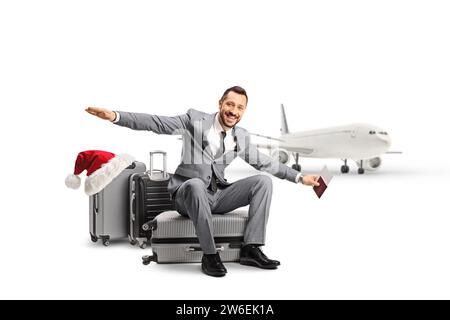 Bussinessman sitzt auf einem Koffer vor einem Flugzeug und spreizt Arme, weihnachtsreisekonzept isoliert auf weißem Hintergrund Stockfoto