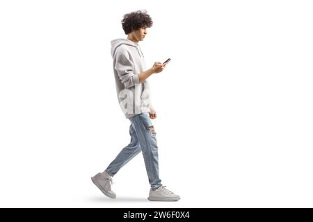 Profilaufnahme in voller Länge von einem Gen z-Mann, der einen grauen Hoodie trägt und mit einem Smartphone auf weißem Hintergrund läuft Stockfoto