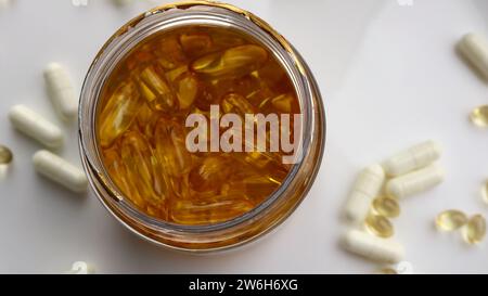 Offenes Glas mit goldenen Kapseln Fischöl, das Omega 3 enthält, Draufsicht auf hellem Hintergrund mit verstreuten Tabletten anderer Vitamine Stockfoto