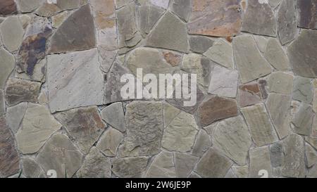 Steintexturwand außen eines Fragments eines Gebäudes oder Zauns mit einer zufälligen Mosaikanordnung aus massiven Fliesen, braun-grauer Hintergrund Stockfoto
