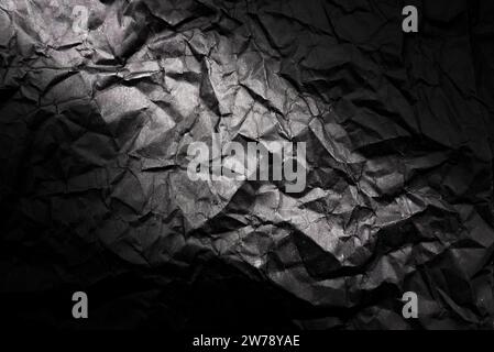 Textur von zerknittertem schwarzem Papier mit Farbverlauf. Dunkler Papierhintergrund mit Falten und Falten Stockfoto