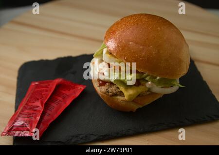 Hausgemachter Burger mit Fleisch, Zwiebeln, Salat, Tomaten und verschiedenen Saucen sowie einigen Ketchup-Paketen Stockfoto