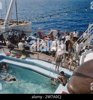 An Bord des Schiffes Jerusalem. Passagiere sonnen sich an Deck in Liegestühlen um einen Swimmingpool herum. Über dem Deck wurde festliche Beleuchtung installiert. Links ein Rettungsboot ca. 1960er Jahre Stockfoto