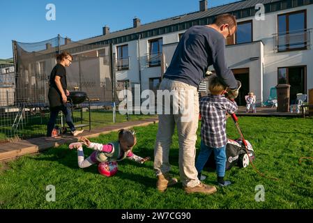 15.09.2018, Polen, Wrzesnia, Wielkopolska - Vater und Sohn, die den Rasen im Garten ihres Reihenhauses mähen, Mutter und Tochter links. 00 Stockfoto