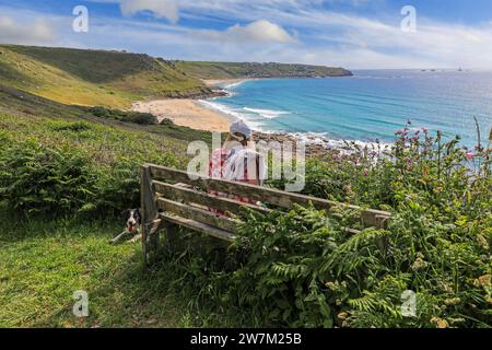 Eine Frau, die auf einer Holzbank mit Blick auf Gwynver Beach oder Gwenver Beach sitzt, Cornwall, Südwestengland, Großbritannien Stockfoto