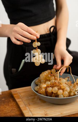 Eine detaillierte Ansicht der Hände und frischen Trauben über einem Küchenbrett. Stockfoto