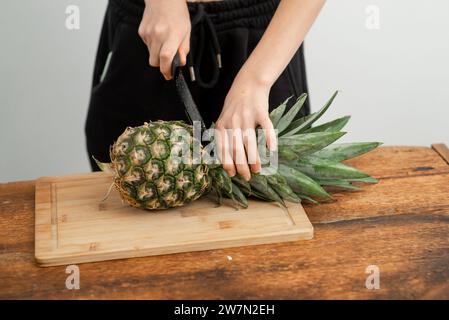 Eine Person, die eine frische Ananas auf einem Bambus Schneidebrett schneidet, Küchenzubereitungskonzept. Stockfoto