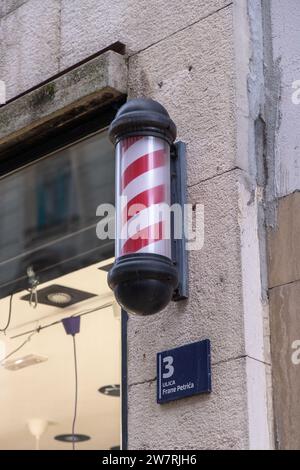 Friseurstange, traditionelles Zeichen für einen Friseurladen: Rotierender Zylinder mit roten Diagonalstreifen (schraubenförmige Streifen); Friseurschild an der Fassade des Friseurshops Stockfoto