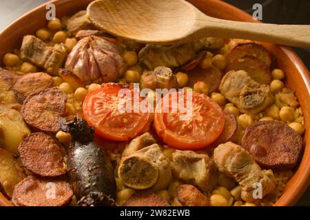 Nahaufnahme eines Auflaufes mit gebackenem Reis, einem typischen valencianischen Gericht mit Blutwurst, Kartoffeln, Kichererbsen, Rippchen neben einem Holzlöffel Stockfoto