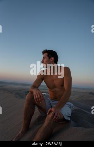 Mann, der auf der Bruneau Sanddüne bei Sonnenuntergang in Idaho sitzt. Die höchsten Sanddünen Nordamerikas im Westen der Vereinigten Staaten. Stockfoto