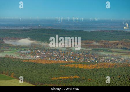 Aus der Vogelperspektive, Nebel über dem Dorf Hullern mit St. Andreas-Kirche, Windturbinenpark im Hintergrund, umgeben von herbstlichen Laubbäumen, Hu Stockfoto