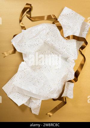 Hochwinkelansicht von zerknittertem Weihnachtspapier und Goldband vor goldenem Hintergrund Stockfoto