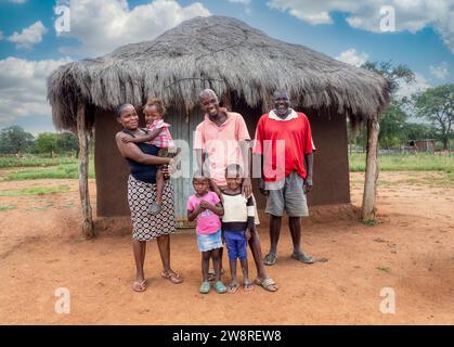 afrikanisches Familiendorf, Vater, Mutter und Großvater zusammen mit den Kindern vor einer Hütte mit Strohdach Stockfoto