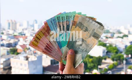 Die Hand des Mannes hält Rupiah-Geld vor dem Hintergrund der Stadt Jakarta. Stockfoto
