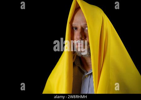 Kahler, bärtiger Mann mit einem gelben Tuch über dem Kopf vor schwarzem Hintergrund. Stockfoto