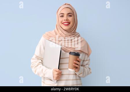Schöne muslimische Frau mit einer Tasse Kaffee und Laptop auf blauem Hintergrund Stockfoto