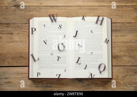 Offenes Buch mit Buchstaben, die auf hölzernem Hintergrund herausfliegen, Draufsicht Stockfoto
