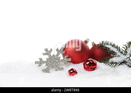 Wunderschöne rote Weihnachtskugeln, Tannenzweig und andere festliche Dekoration auf Schnee vor weißem Hintergrund Stockfoto