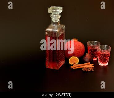 Feigen-Granatapfellikör, starker hausgemachter Alkohol mit Zimt, Anis in zwei Gläsern und eine Kristallkaraffe auf schwarzem Hintergrund, neben Reifen Früchten Stockfoto