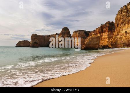 Schaumiges Wasser an einem Sandstrand mit großen Felsen an einem Wintertag im Süden Portugals. Stockfoto