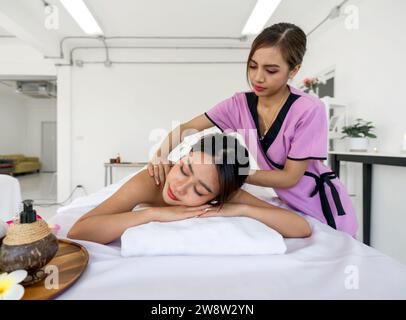 Eine professionelle Masseurin gibt einer entspannten Frau, die mit weichen Handtüchern bedeckt ist, aufmerksam eine therapeutische Massage. Atmosphäre in ruhiger Atmosphäre in einem Spa. Stockfoto