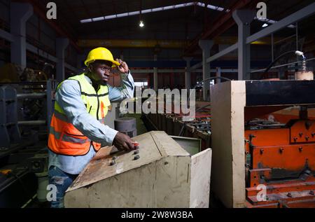 Ein dunkelhäutiger Mann arbeitet konzentriert und fleißig an einer Maschine in einer geschäftigen Fabrik. Stockfoto