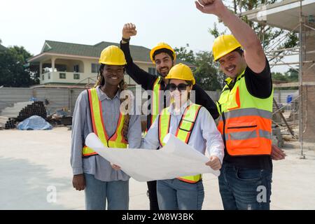 Einige Bauherren halten Pläne an ihrem Arbeitsplatz. Erfolg Feiern. HardHat Bauarbeiter heben die Hand hoch und markieren einen siegreichen Moment. Stockfoto