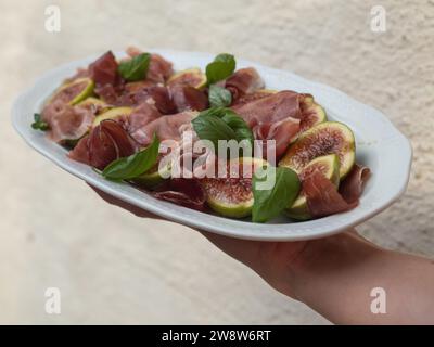 Horizontale Nahaufnahme einer Hand, die einen Teller Feigen- und Prosciutto-Salat hält. Stockfoto
