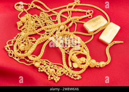 Viele goldene Ketten und Goldbarren auf rotem Samthintergrund. Stockfoto