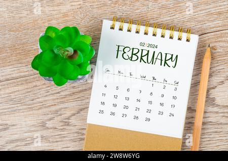 Februar 2024 monatlicher Schreibtischkalender und Bleistift mit Pflanztopf Dekoration auf hölzernem Hintergrund. Stockfoto