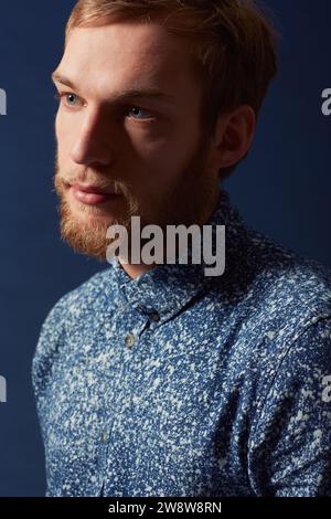 Mann, Mode und seriöses Gesicht im Studio mit einzigartigem Stil, Denim und trendy auf blauem Hintergrund. Irisches Modell mit Hipster-Bart, rotem Haar und lässigem Haar Stockfoto