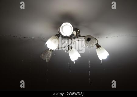 Aufgrund eines Rohrbruchs gab es eine Überschwemmung in der Wohnung oben und Wasser fließt von der Decke und entlang des Kronleuchters und entlang der Decke. Stockfoto