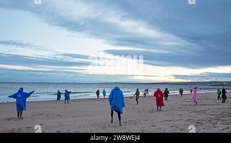 Portobello, Edinburgh, Schottland, Großbritannien. 22. Dezember 2023. Wintersonnenwende, „Achtsamkeit Bewegung Silent Disco Body Centred Coaching“ mit „Move to Feel“ neben dem Firth of Forth, „eine kreative achtsame Bewegungspraxis, ein unterhaltsames therapeutisches Ereignis, bei dem die Intelligenz des Körpers durch Fühlen, Fühlen, Erkunden, Bewegen, Gestalten und Verbinden zusammengeführt wird“. Quelle: Archwhite/Alamy Live News. Stockfoto