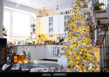 Weihnachtliche Einrichtung in weißer Küche, modernes Innenleben im Dorf mit einem schneebedeckten Weihnachtsbaum und Feenlichtern. Neujahr, Weihnachtsstimmung, gemütliches Zuhause, M Stockfoto