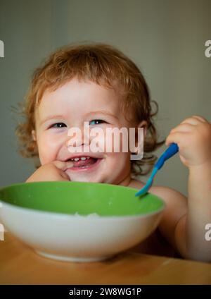 Lächelndes Baby Essen. Lustige Baby Essen selbst mit einem Löffel in der Küche. Gesunde Ernährung für Kinder. Starten Kind essen Nahrung. Stockfoto