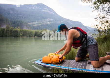 Der SUP Paddle Boarder sichert trockene Taschen an Bord. Stockfoto