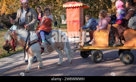 Belgrad, Serbien, 12. November 2023: Mann, der ein Pony führt und einen Wagen zieht, mit einem kleinen Mädchen auf dem Rücken Stockfoto