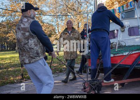 Belgrad, Serbien, 12. November 2023: Eine Gruppe von Menschen zieht ein altes Metallboot, das auf einem Anhänger auf dem Zemun-Kai neben der Donau montiert ist Stockfoto