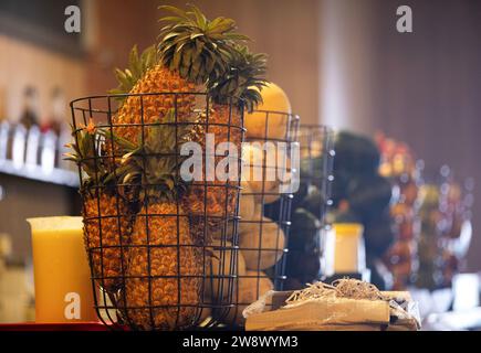 Ein Haufen reifer Ananas sitzt in einem rustikalen Drahtkorb auf einem Holztisch Stockfoto